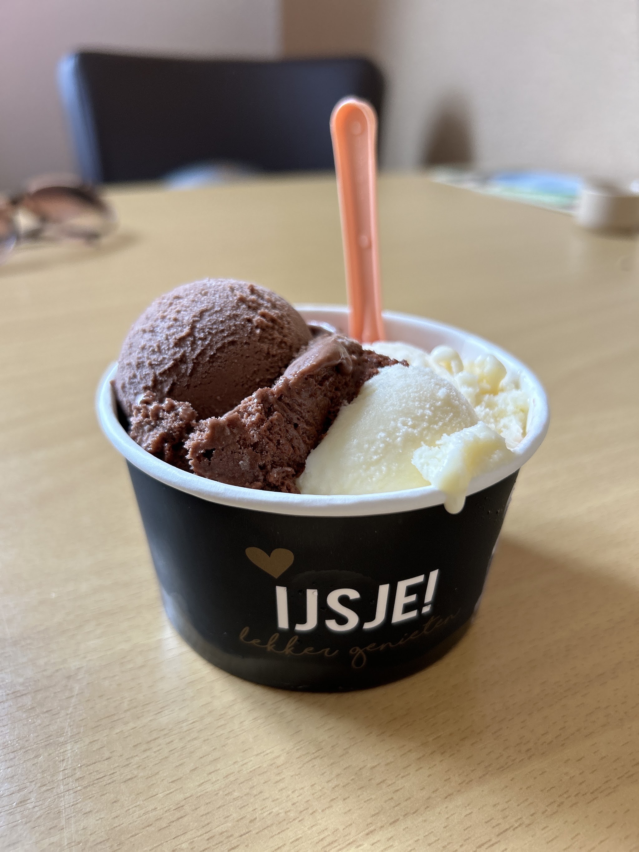 Een afhaalbakje met een bol chocolade-ijs en een bol vanille-ijs