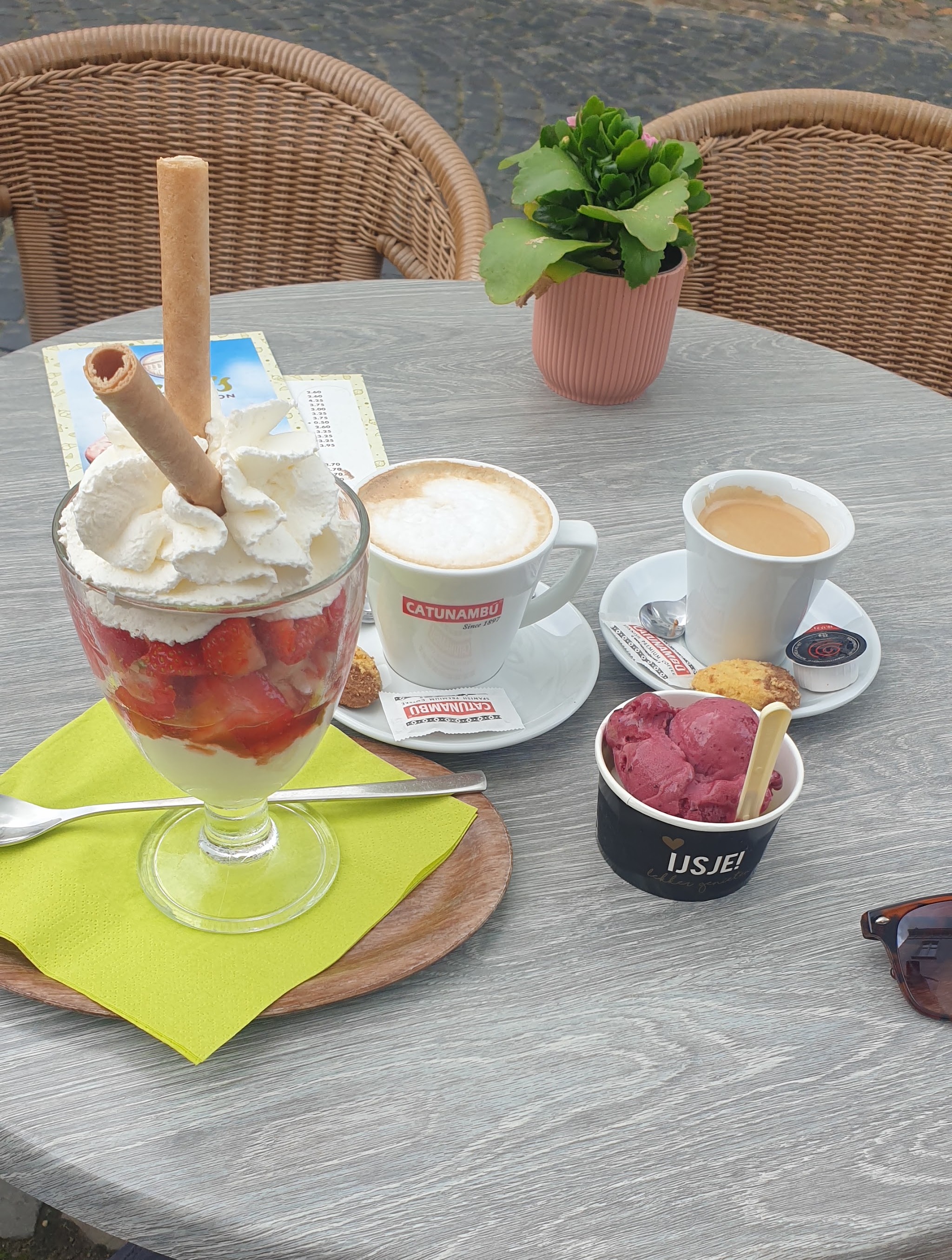 Een terrastafel met een aardbeiencoupe, een cappuccino, een espresso en een bakje sorbet